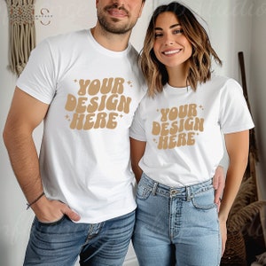 May include: Two white t-shirts with the text "Your Design Here" in brown, retro-style lettering. The shirts are worn by two people standing next to each other.