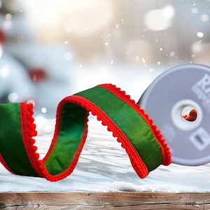 May include: A festive image featuring a green ribbon with red trim and a decorative edge, alongside a silver disc with the text "RAZ Imports". The ribbon is curled, suggesting it's for wrapping gifts or decorations. The background is blurred with a snowy effect.