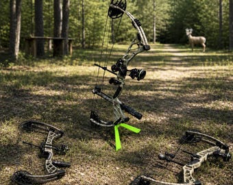 Peut inclure: Trois arcs à poulies avec un motif camouflage et des détails noirs et verts sont posés sur le sol dans une forêt. Un arc est droit, soutenu par un support vert fluo. Un cerf est visible à l'arrière-plan.