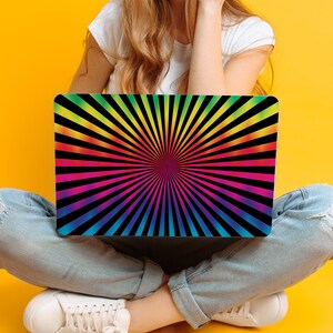 May include: A person is sitting with a laptop computer that has a rainbow colored sunburst design on the screen.