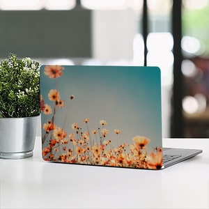 May include: A laptop computer with a floral design on the lid. The design features a field of orange and yellow flowers against a blue sky.
