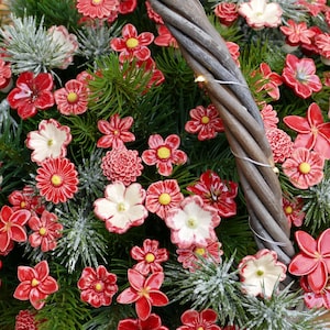 Könnte beinhalten: Ein Weidenkorb gefüllt mit roten und weißen Keramikblumen, umgeben von grünen Kiefernästen mit einer Schneedecke.