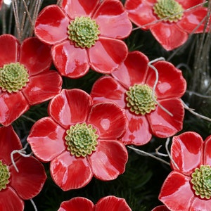 Könnte beinhalten: Nahaufnahme mehrerer glänzender roter Keramikblumenornamente mit grünen Zentren. Die Blütenblätter sind leuchtend rot und die Zentren haben ein strukturiertes, grünes Aussehen. Die Blumen sind mit silbernen und weißen dekorativen Akzenten angeordnet.