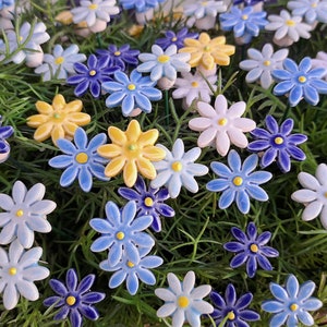 Könnte beinhalten: Sortiment an Keramik-Gänseblümchen in den Farben Blau, Gelb und Weiß. Die Blumen sind in einem Bett aus grünem Gras angeordnet.