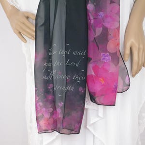 May include: A sheer scarf with a floral design in shades of pink and purple. The scarf has a black border and features the text "They that wait upon the Lord shall renew their strength" in white script.
