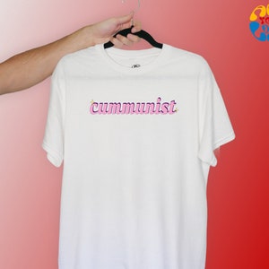 May include: White t-shirt with the word "communist" written in pink letters with a yellow star above the first letter.
