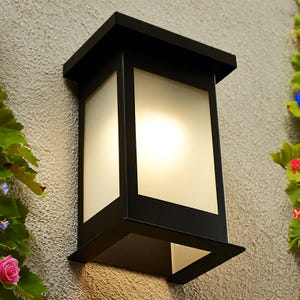 May include: Black outdoor wall light fixture with a frosted glass panel. The light is mounted on a beige wall.