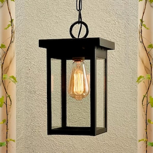 Könnte beinhalten: Schwarze Metall-Außenlaterne mit einer klaren Glasscheibe und einer einzelnen Glühbirne. Die Laterne hängt an einer Kette.