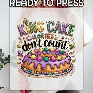 May include: A white t-shirt with a colorful graphic design of a king cake with the text "King Cake Calories don't count".