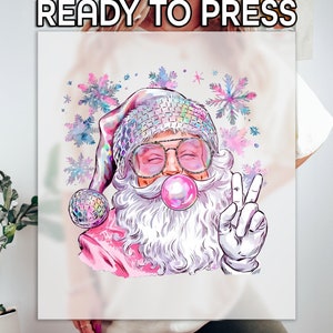 May include: A colorful graphic of Santa Claus wearing sunglasses, a disco ball hat, and blowing a bubblegum bubble. He is giving a peace sign with his gloved hand. The words "READY TO PRESS" are at the top.