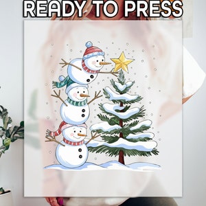 May include: Three snowmen are stacked on top of each other, with the top snowman reaching for a gold star on top of a snow-covered Christmas tree. The snowmen are wearing colorful hats and scarves.