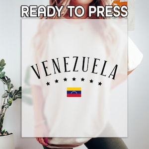 May include: Cream-colored t-shirt with the word "VENEZUELA" in a black, arched font, with seven black stars below and the Venezuelan flag. The text "READY TO PRESS" is at the top.