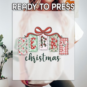 May include: A white t-shirt with the words "MERRY christmas" in a festive design. The letters are decorated with patterns like stripes, polka dots, and plaid, and are topped with a red bow. The words "READY TO PRESS" are at the top.