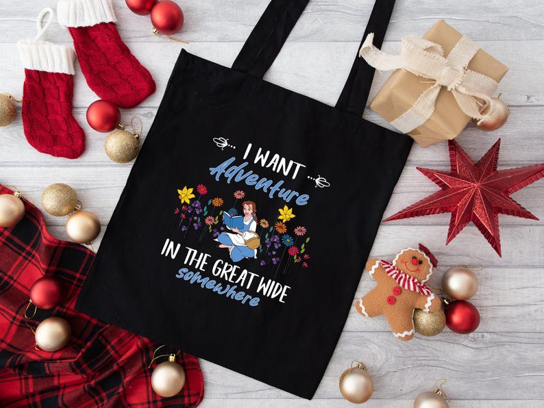 May include: Black tote bag with white text that reads "I want adventure in the great wide somewhere". The text is surrounded by colourful flowers and a cartoon illustration of a girl reading a book.