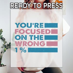May include: White t-shirt with the text "You're focused on the wrong 1%" in blue and pink lettering with a blue and pink striped background.