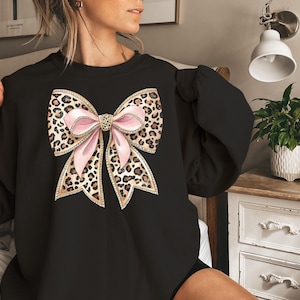 May include: Black sweatshirt with a large pink and brown leopard print bow with rhinestones on the front.
