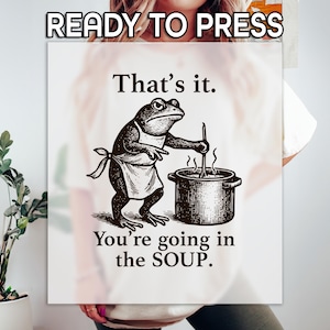 May include: White sign with a frog illustration wearing an apron, stirring a pot. Text reads "That's it. You're going in the SOUP." The words "READY TO PRESS" are at the top. The image has a vintage, humorous style.