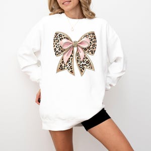 May include: White sweatshirt with a large pink and brown leopard print bow with gold accents.