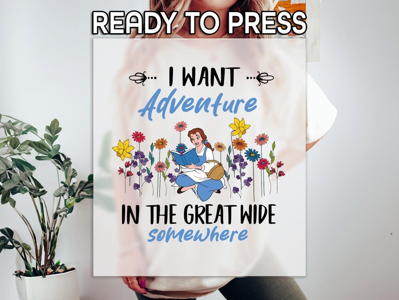 May include: A white t-shirt with a graphic design featuring Belle from Beauty and the Beast reading a book in a field of flowers. The text reads "... I WANT ... Adventure in the great wide Somewhere".
