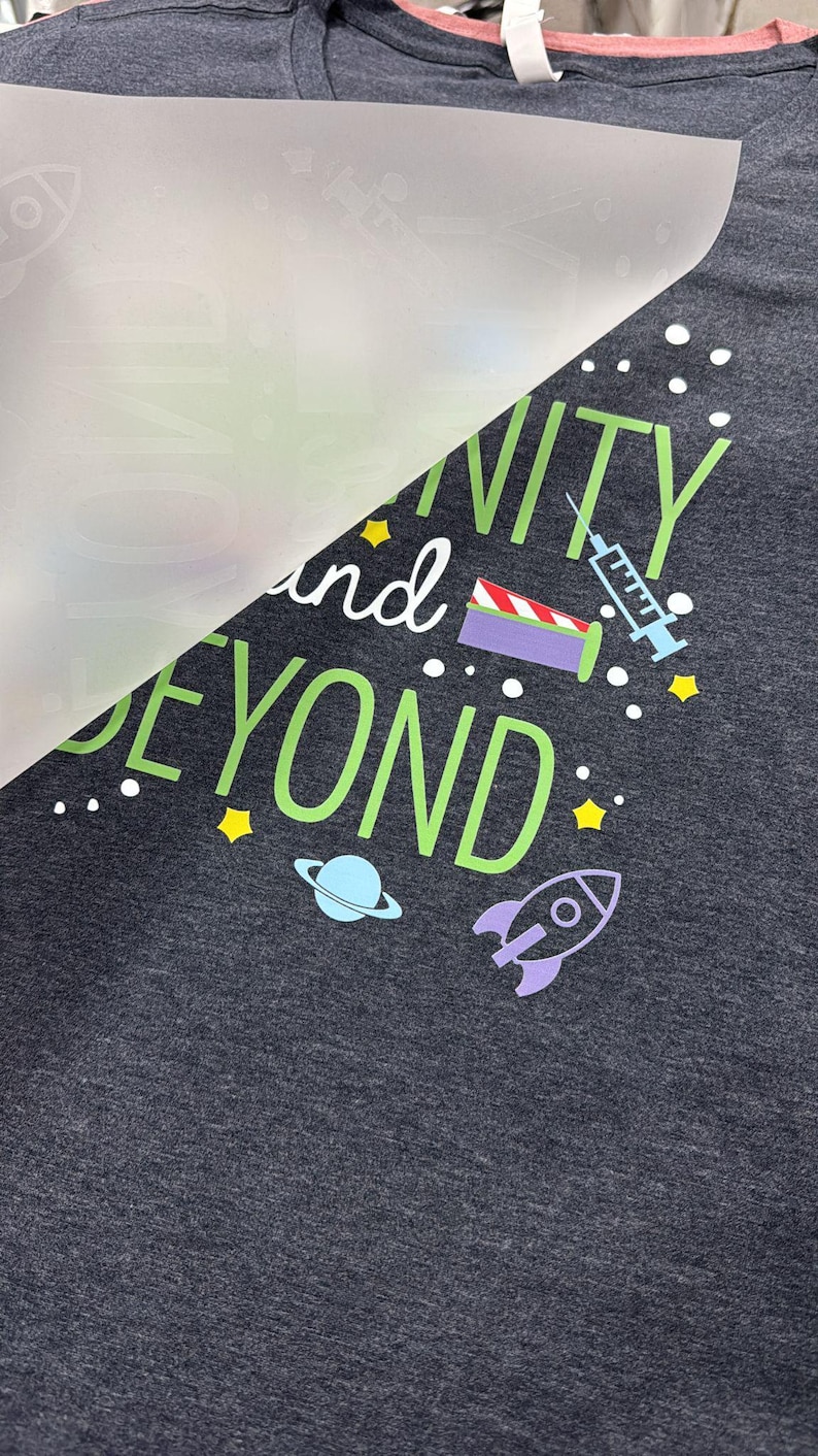 May include: A dark gray t-shirt with a green and white design that says "Infinity and Beyond" with a rocket ship, a planet, and a syringe.