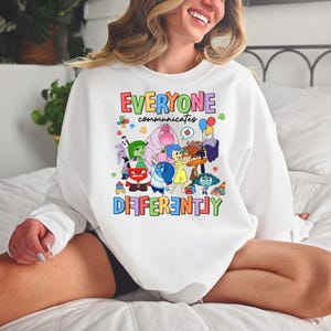 May include: White sweatshirt with a colorful graphic of characters from the movie Inside Out. The text "Everyone communicates differently" is printed in rainbow colors.