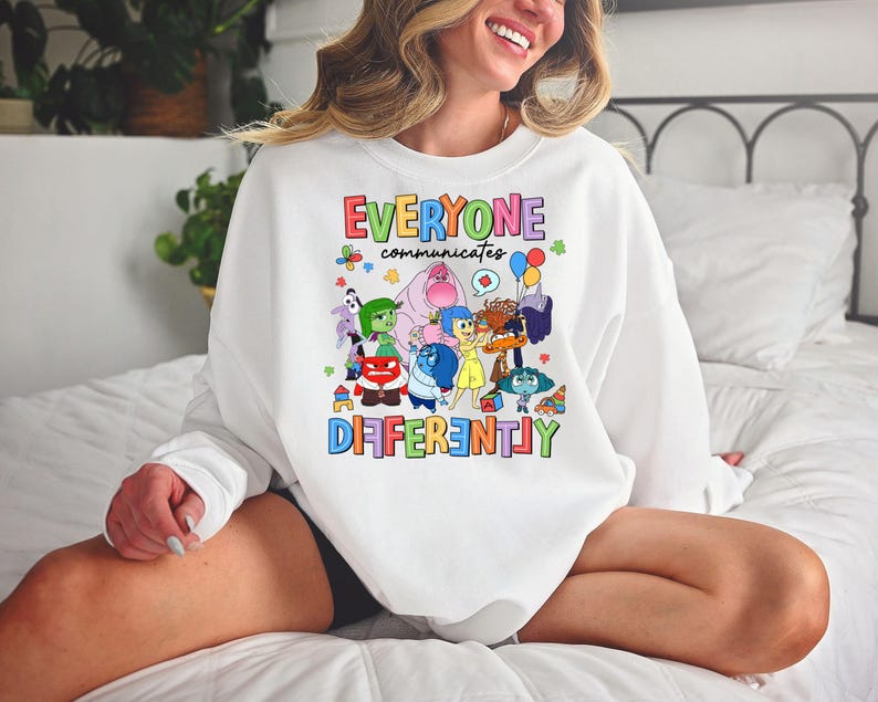 May include: White sweatshirt with a colorful graphic of characters from the movie Inside Out. The text "Everyone communicates differently" is printed in rainbow colors.