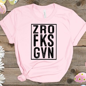 May include: Pink t-shirt with a black square graphic that says "ZRO FKS GVN".