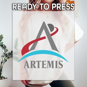 May include: White t-shirt with the text "READY TO PRESS" at the top. The shirt features a logo with a gray letter "A", a red and gray curved line, and a blue curved line with the word "ARTEMIS" below.