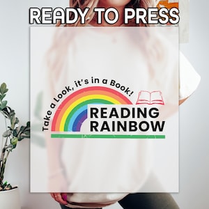 May include: White t-shirt with a colorful rainbow design and the words "Take a Look, it's in a Book!" and "Reading Rainbow". The design includes an open book graphic and the text "READY TO PRESS" at the top.