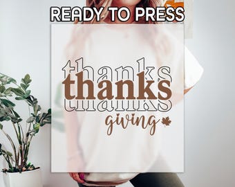 May include: A white sublimation transfer with the words "thanks giving" in a brown and black font, with a small maple leaf graphic. The words "READY TO PRESS" are at the top.