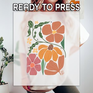 May include: White t-shirt with a floral design in shades of orange, pink, and green. The design features stylized flowers and leaves, with the text "READY TO PRESS" at the top. The design is centered on the shirt.