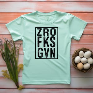 May include: A light green t-shirt with a black box containing the text "ZRO FKS GVN" in a distressed font.