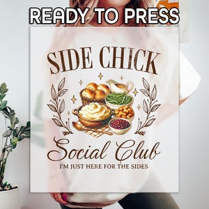 May include: White t-shirt with a graphic that reads "SIDE CHICK Social Club" in brown script. The graphic features illustrations of various side dishes, including mashed potatoes, green beans, and rolls. The text "I'M JUST HERE FOR THE SIDES" is also included.