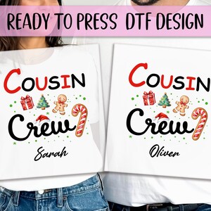 May include: White t-shirts with a Christmas design. The shirts read "Cousin Crew" in black and red, with festive graphics like a gingerbread man, candy cane, and Christmas tree. One shirt says "Sarah" and the other says "Oliver".