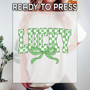 May include: A white t-shirt with a green checkered design that says "LUCKY" with a green bow underneath.