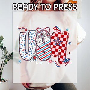May include: A graphic design with the letters "USA" in red, white, and blue, with star and stripe patterns. The design is on a white background and includes the text "READY TO PRESS".