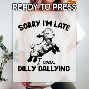 May include: White t-shirt with black text that reads "Sorry I'm Late I was Dilly Dallying". A black and white illustration of a lamb jumping is above the text.