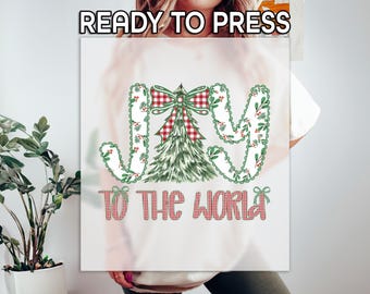 May include: A white graphic featuring the words "JOY TO THE WORLD" in a festive design. The word "JOY" is in a decorative font with green and red accents. A Christmas tree and bow are in the center.