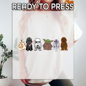 May include: A white t-shirt with a print of Star Wars characters, including Darth Vader, R2-D2, Chewbacca, and Yoda. The text "READY TO PRESS" is printed at the top of the image.
