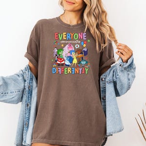 May include: A brown t-shirt with a graphic of characters from the movie Inside Out. The text on the shirt reads "Everyone Communicates Differently".