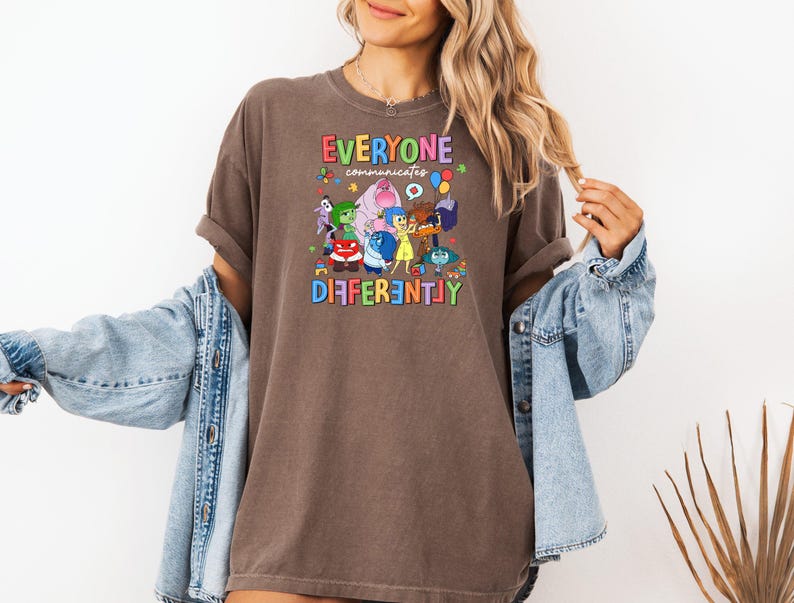 May include: A brown t-shirt with a graphic of characters from the movie Inside Out. The text on the shirt reads "Everyone Communicates Differently".