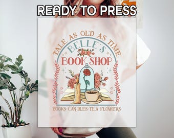 May include: A white t-shirt with a design featuring a book shop with the text "Tale as old as time Belle's Book Shop" and "Books Candles Tea Flowers".