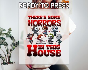 May include: White t-shirt with the text "THERE'S SOME HORRORS IN THIS HOUSE" in red and black. The design features cartoon versions of horror movie characters. The words "READY TO PRESS" are at the top.