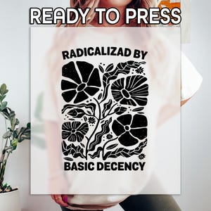 May include: White t-shirt with a black floral design and the text "RADICALIZED BY BASIC DECENCY". The design features stylized flowers and leaves. The words "READY TO PRESS" are at the top.