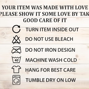 May include: A set of laundry care instructions on a wooden background. The instructions include: turn item inside out, do not use bleach, do not iron design, machine wash cold, hang for best care, and tumble dry on low.