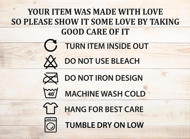 May include: A set of laundry care instructions on a wooden background. The instructions include: turn item inside out, do not use bleach, do not iron design, machine wash cold, hang for best care, and tumble dry on low.