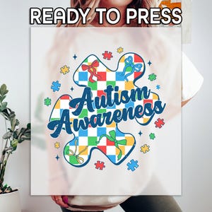 May include: White t-shirt with a colorful puzzle piece design that says "Autism Awareness".