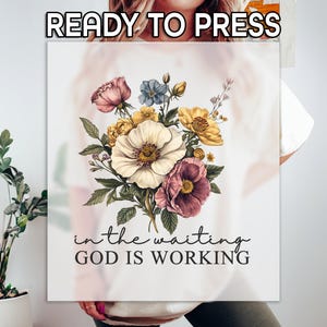 May include: A white t-shirt with a floral design and the text "in the waiting GOD IS WORKING".