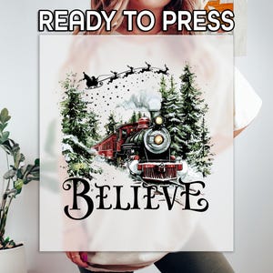 May include: A graphic featuring a vintage train with a red carriage, snow-covered evergreen trees, and Santa's sleigh. The word "BELIEVE" is written in a decorative font. The text "READY TO PRESS" is at the top.
