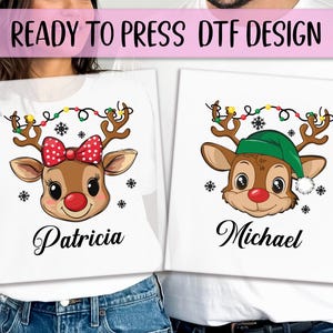 May include: Two white t-shirts with Christmas reindeer designs. One reindeer has a red bow and the name "Patricia" below. The other reindeer has a green hat and the name "Michael" below. Both reindeer have festive lights on their antlers.
